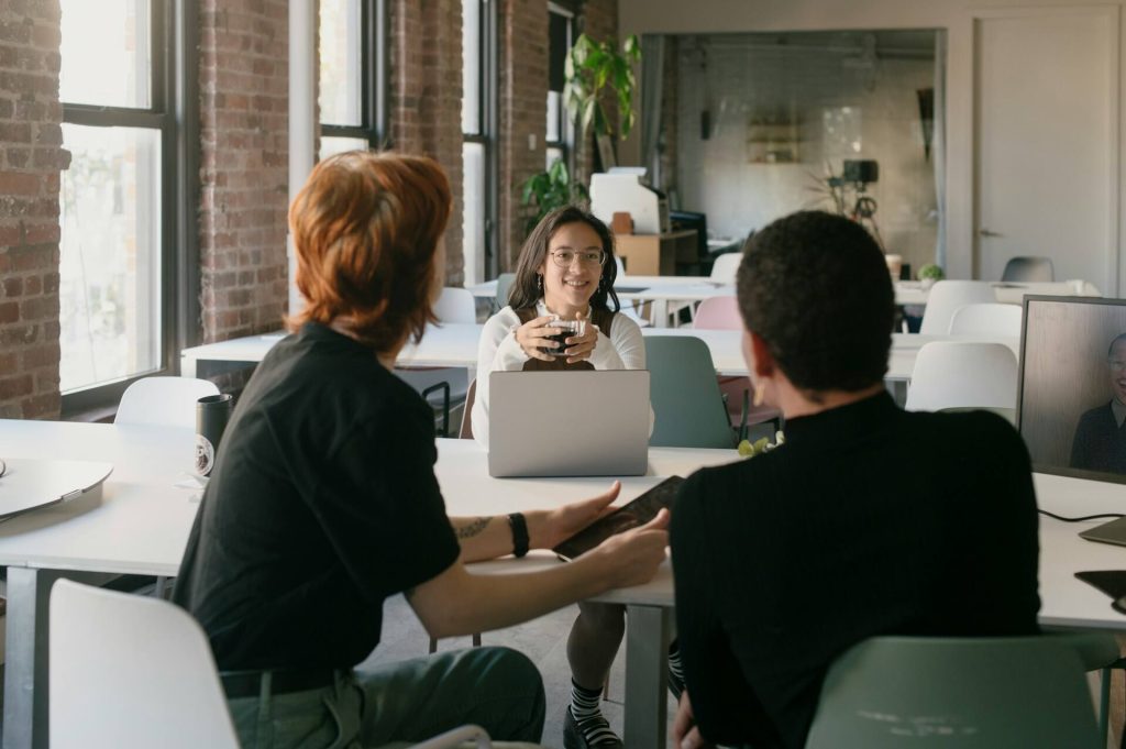 Three young workers are chatting in a cafeteria with a computer open.